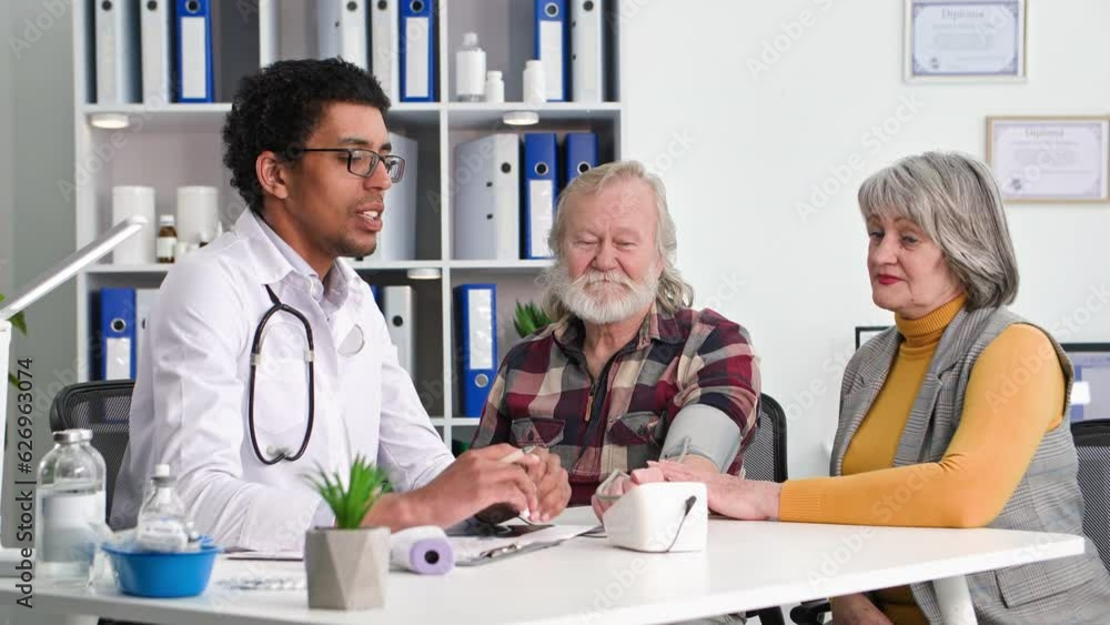 care health, black doctor will measure pressure with modern tonometer to an elderly man at a reception with his wife in medical office care health, black doctor will measure pressure with modern tonometer to an elderly man at a reception with his wife in medical office