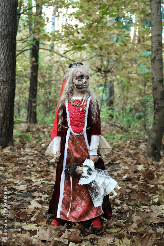 Girl child posing in the forest in a medieval dress in the image of a dead princess. Girl holding a doll Girl child posing in the forest in a medieval dress in the image of a dead princess. Girl holding a doll