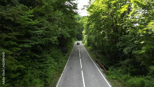 The car drives along a forest road on the sides grow trees. Aerial view.