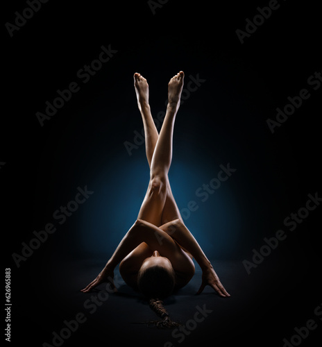 Beautiful fitness girl with a great figure flexing her perfect body in a yoga pose at the studio. Spider pose with a vertical light and studio dark background