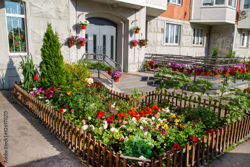 Flowerbeds of bright flowers and various plants in front of the entrance of a residential building. Agriculture Landscaping landscaping of cities. #626970213