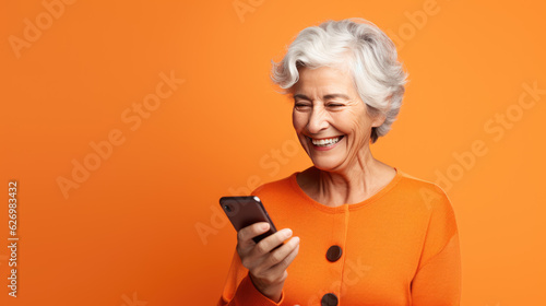 An elderly woman smiling with her phone against an orange background.