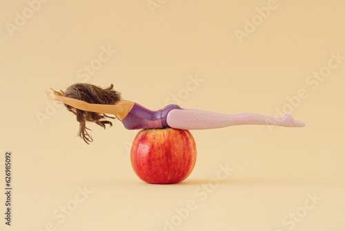 Girl and red apple on sandy color background. Minimal surreal, creative concept of ballet, Pilates, fitness workout and healthy lifestyle, flexibility and body awareness . Copy space.