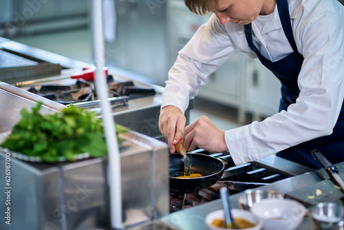 A single boy chef try to fire egg into the pan on gas strove in kitchen.