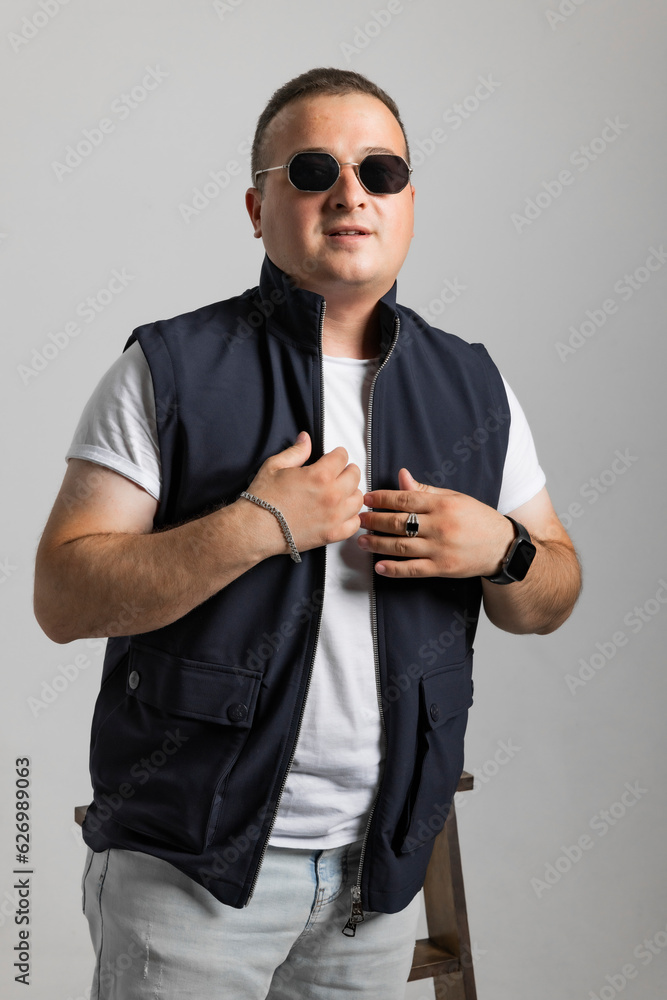A cheerful young man model in a sleeveless regular solid jacket and a black sunglass posing in multiple different styles over white background with dimensions of width 5464 p and height 8192 p
