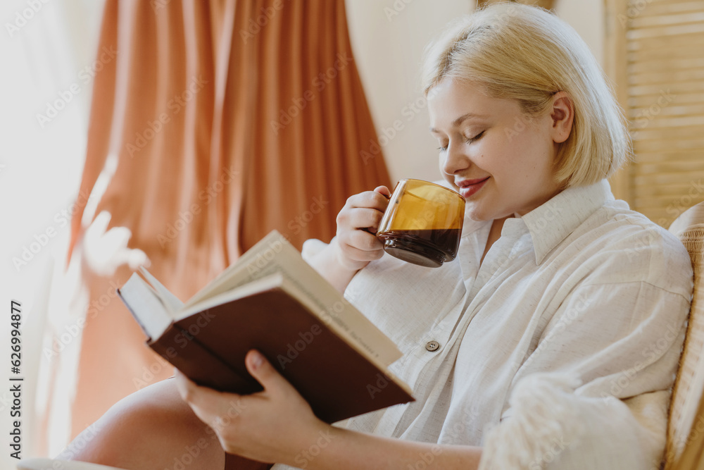 Adorable young woman with eyes closed drinking coffee and reading book while relaxing on chair. Adorable young woman with eyes closed drinking coffee and reading book while relaxing on chair.