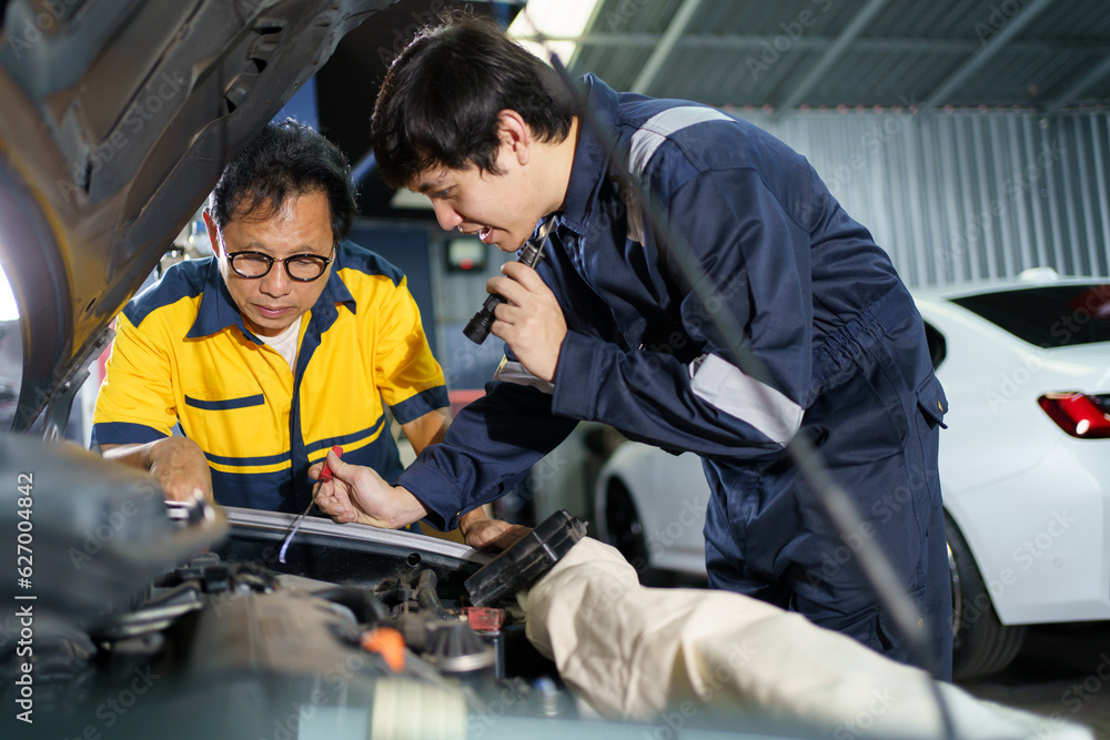 Team of vehicle technicians checking and measuring a vehicle oil engine or engine lubricant level by using oil stick indicator. Senior professional repairman inspecting an oil engine in an old car. Team of vehicle technicians checking and measuring a vehicle oil engine or engine lubricant level by using oil stick indicator. Senior professional repairman inspecting an oil engine in an old car.