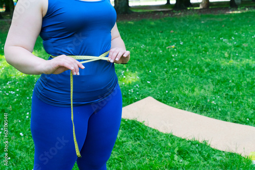Woman and sports, exercise for weight loss in the fresh air. Curvy plus size woman measuring her waist after sport routine in city park, close up view