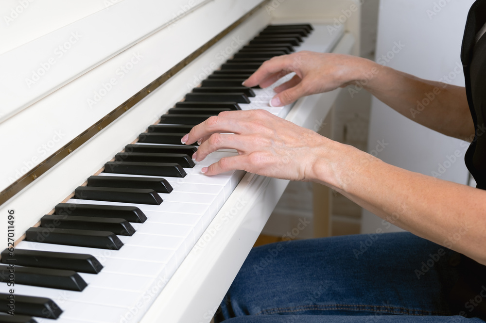 Fototapeta premium Close-up of female hands on piano keys. A woman with French manicure plays the piano. Musician with musical instrument learning music.