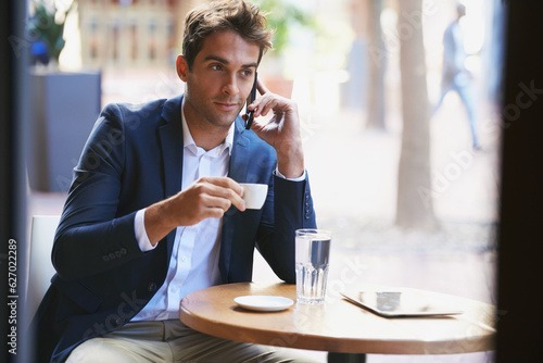 Business even when on break. Shot of a young businessman enjoying a cup of coffee and talking on the phone.