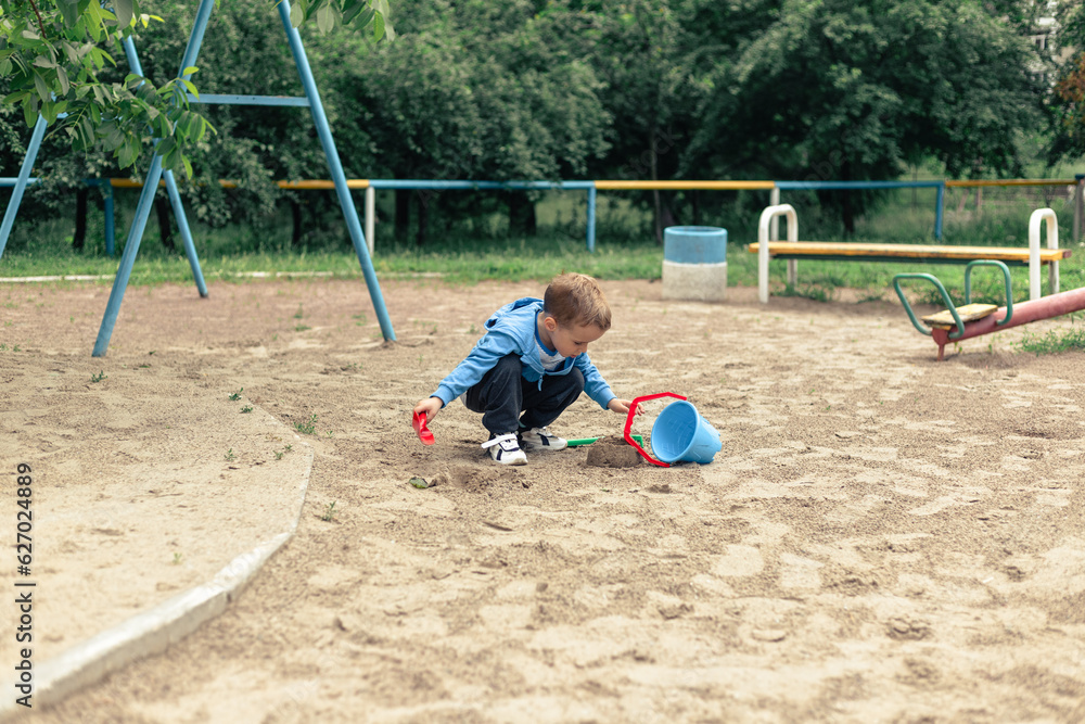 A little boy plays in a large wide sandbox on the playground A little boy plays in a large wide sandbox on the playground