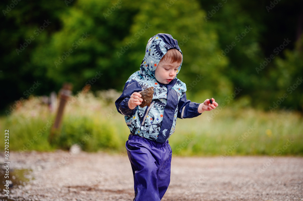 Little toddler boy in waterproof wearing playing in puddle with water Little toddler boy in waterproof wearing playing in puddle with water