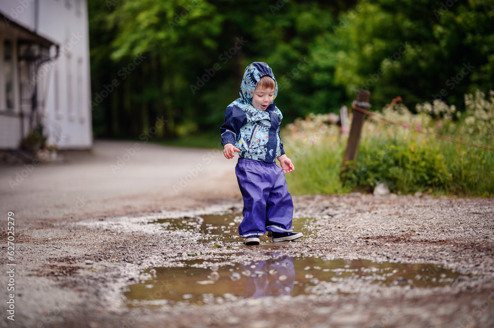 Little toddler boy in waterproof wearing playing in puddle with water Little toddler boy in waterproof wearing playing in puddle with water