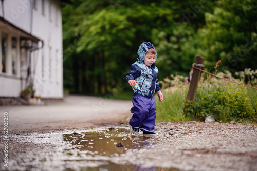 Little toddler boy in waterproof wearing playing in puddle with water