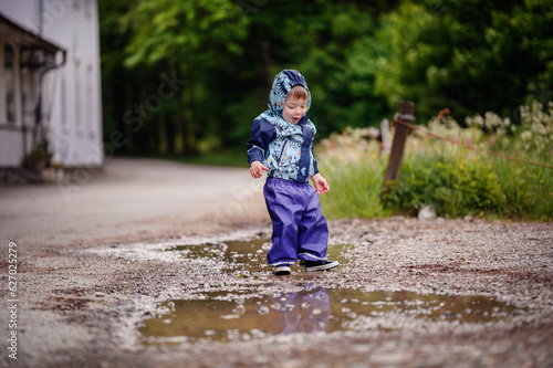 Little toddler boy in waterproof wearing playing in puddle with water