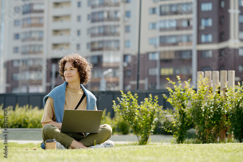 Canvas Print Young smiling woman with laptop sitting on green grass in park on sunny summer d