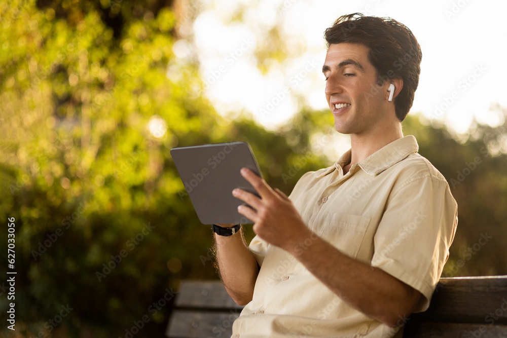 Cheerful man enjoying nice podcast, resting on bench at park