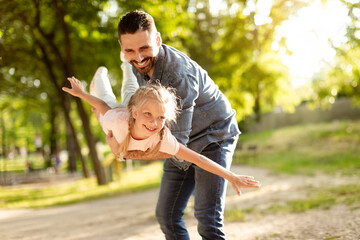 Carefree summer moment. Excited father holding his cute daughter on hands, playful girl enjoying freedom of flying