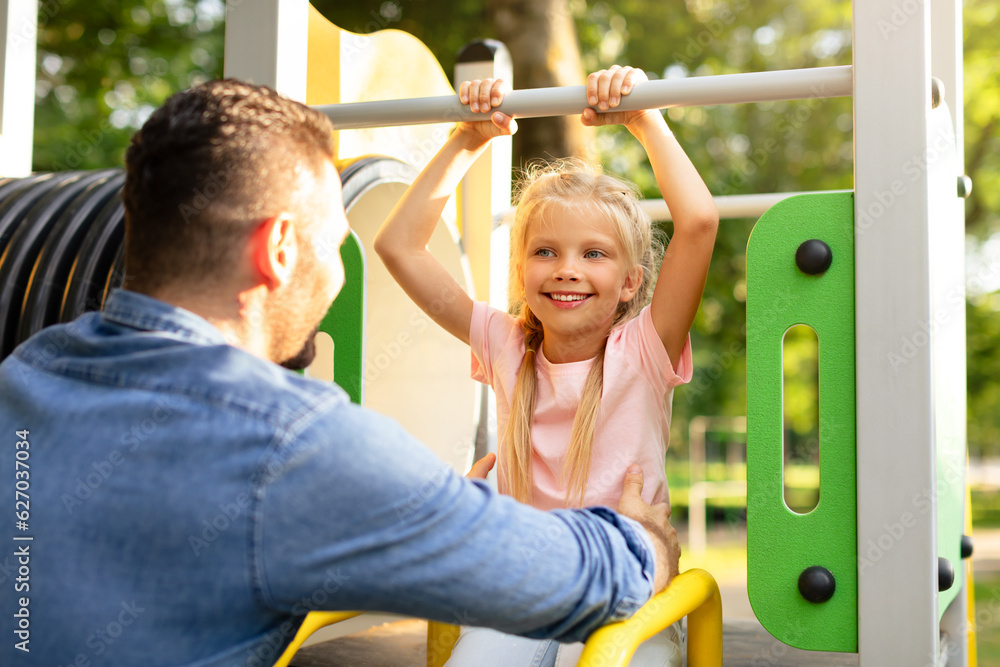 Obraz premium Tales from the playground. Father playing with his little happy daughter in the park, girl sitting on slide