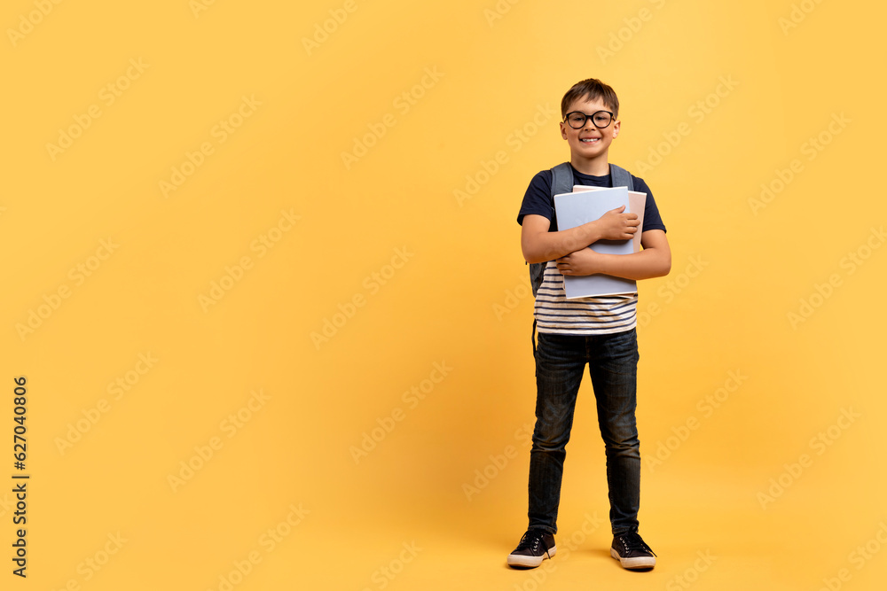 Cheerful preteen boy schooler with backpack and notebooks on yellow Cheerful preteen boy schooler with backpack and notebooks on yellow
