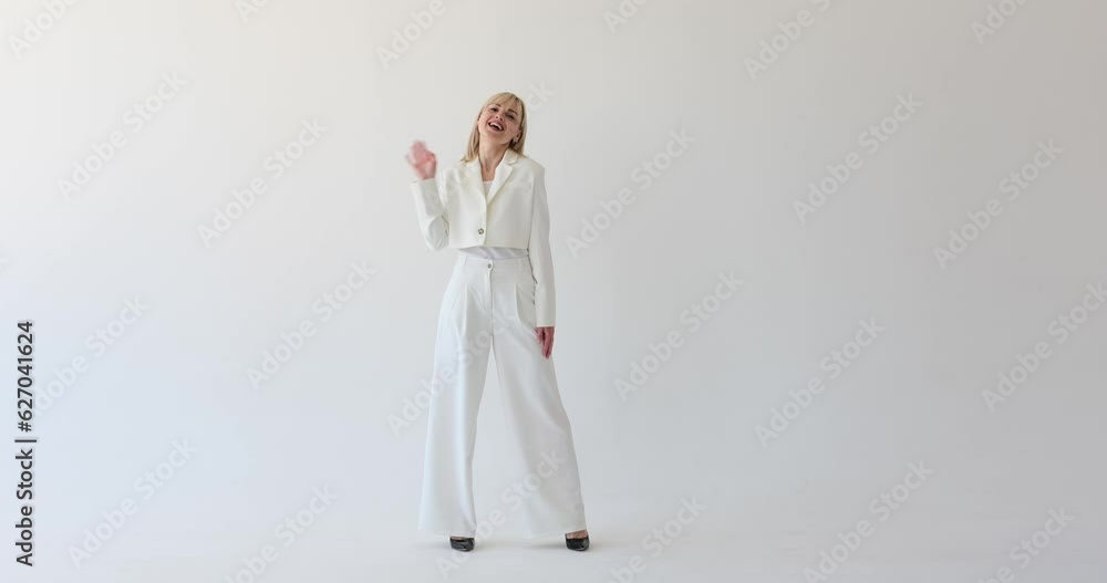 A joyful woman standing on a white background, happily waving her hand with a bright smile. Her infectious happiness radiates as she greets with a friendly wave. A joyful woman standing on a white background, happily waving her hand with a bright smile. Her infectious happiness radiates as she greets with a friendly wave.
