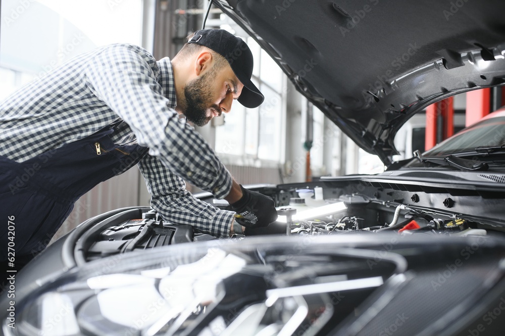 Mechanic examining under hood of car at the repair garage Mechanic examining under hood of car at the repair garage
