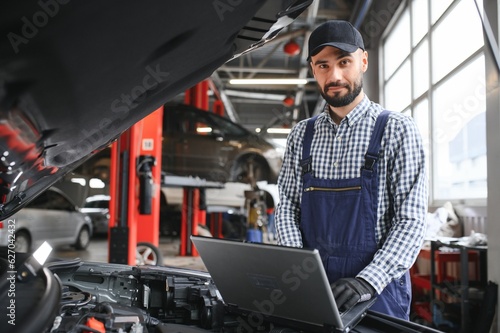 Smiling mechanic using a laptop pc at the repair garage. © Serhii