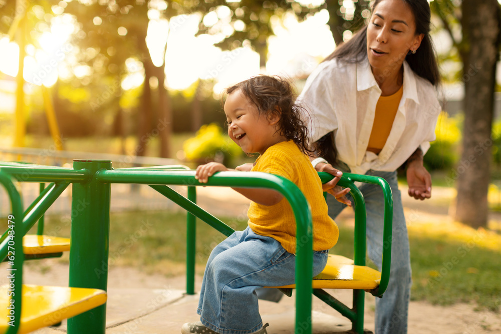 Obraz premium Happy Asian Baby Riding On Carousel Playing With Mother Outdoor