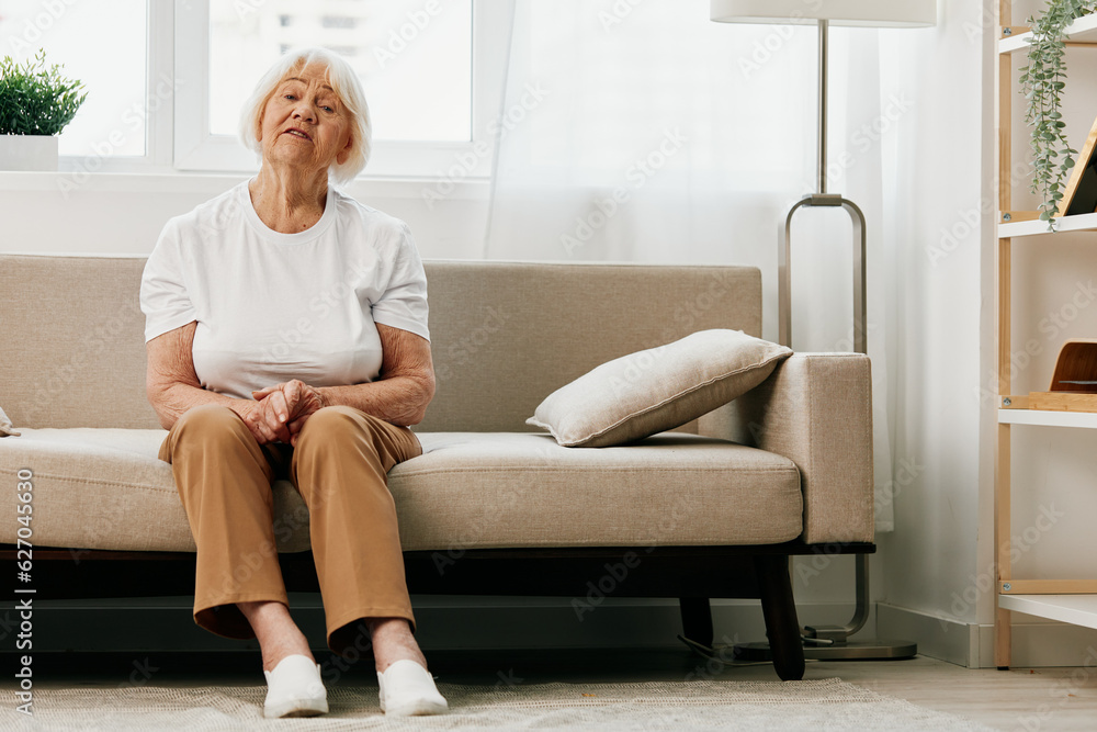 Elderly woman severe abdominal pain sitting on the sofa, health problems in old age, poor quality of life. Grandmother with gray hair holding her stomach, poisoning, problems with stool. Elderly woman severe abdominal pain sitting on the sofa, health problems in old age, poor quality of life. Grandmother with gray hair holding her stomach, poisoning, problems with stool.