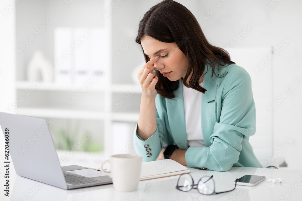 Unhappy tired millennial caucasian lady in suit rest at workplace with computer, suffer from headache Unhappy tired millennial caucasian lady in suit rest at workplace with computer, suffer from headache