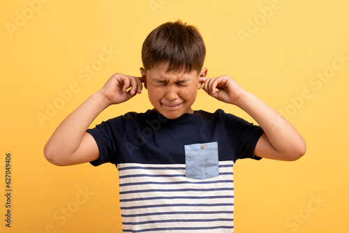 Angry unhappy irritated boy covering ears isolated over yellow background Fototapet