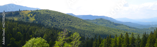 Range of mountains covered in green trees. The sky is blue with a few clouds.