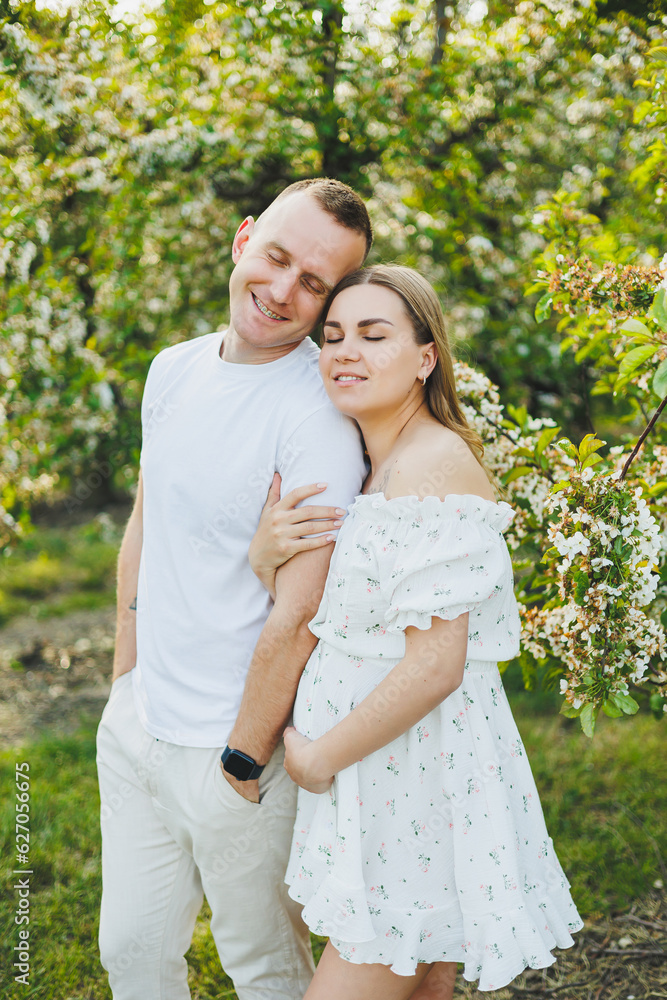 Beautiful young couple in spring garden. Beauty lifestyle family concept. A happy mother is expecting a baby. A happy young couple in a blooming garden Beautiful young couple in spring garden. Beauty lifestyle family concept. A happy mother is expecting a baby. A happy young couple in a blooming garden