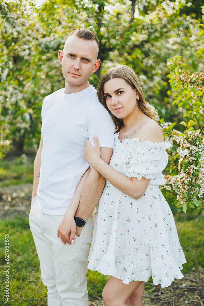 Beautiful young couple in spring garden. Beauty lifestyle family concept. A happy mother is expecting a baby. A happy young couple in a blooming garden