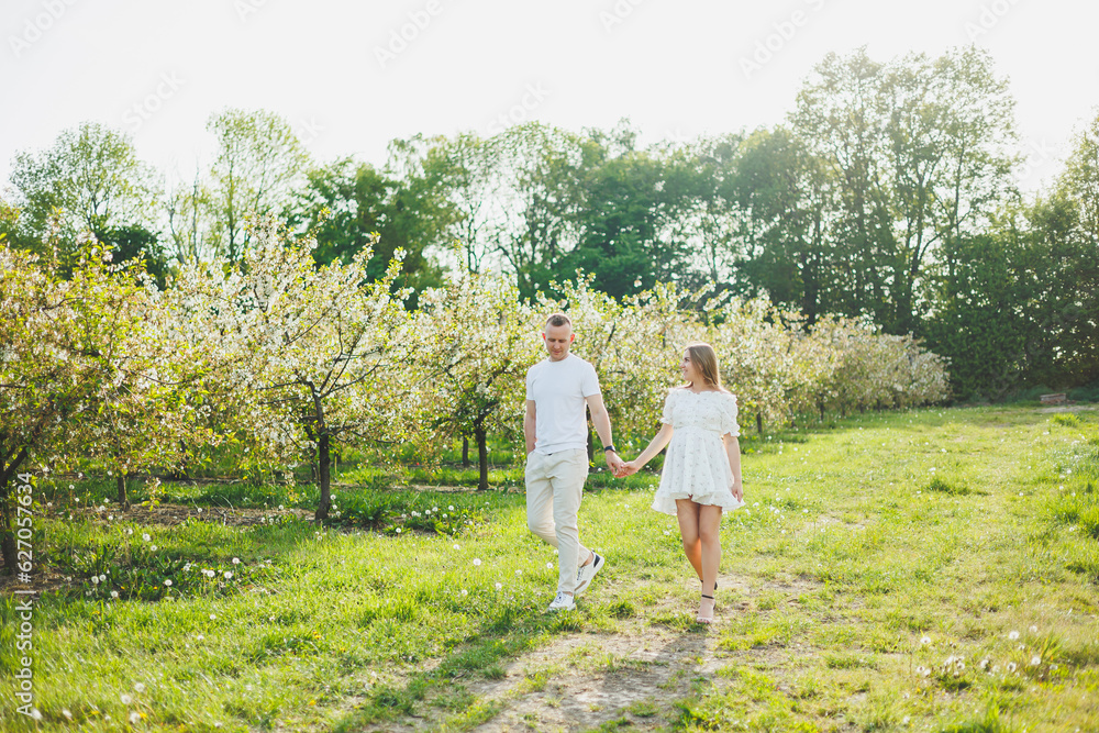 A young happy couple in anticipation of pregnancy walks through a blooming garden. Couple in love in blossoming apple trees. A young happy couple in anticipation of pregnancy walks through a blooming garden. Couple in love in blossoming apple trees.
