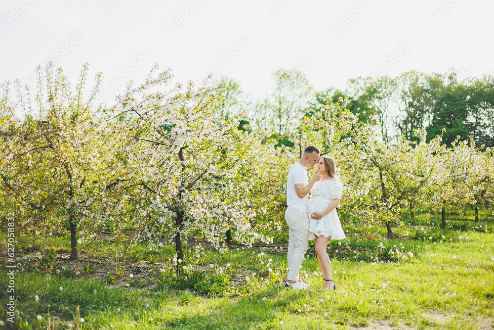 The concept of happy family relationships. A young happy couple in anticipation of pregnancy walks through a blooming garden. Couple in love in blossoming apple trees.