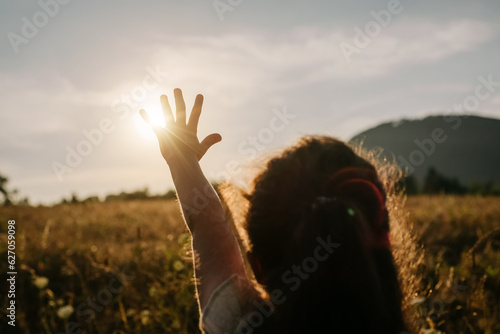 Silhouette of preteen girl raising hand over sunset sky, enjoying life and nature. Child on summer field enjoying sunlight. Little kid in warm sunlight rays. Air, environment concept. Dream of flying
