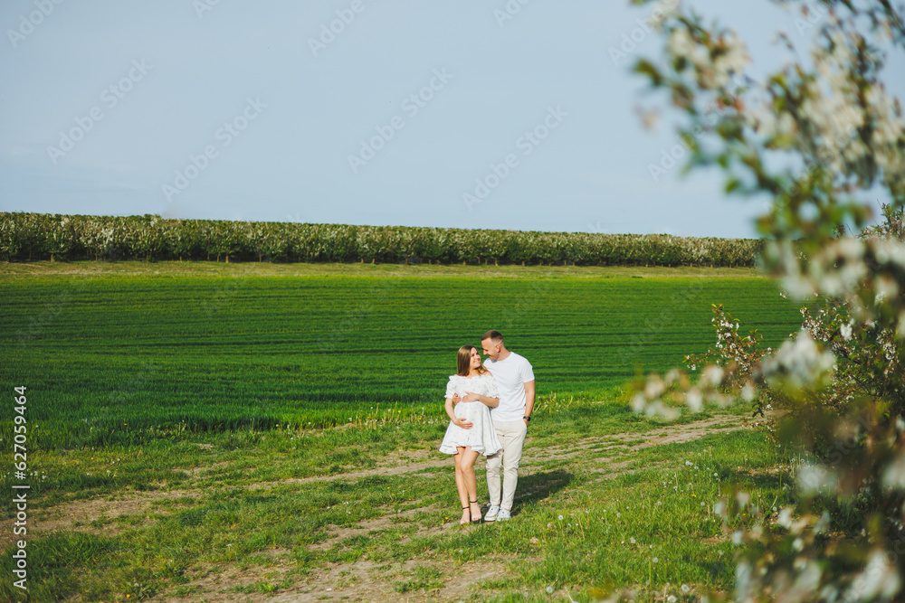 The concept of happy family relationships. A young happy couple in anticipation of pregnancy walks through a blooming garden. Couple in love in blossoming apple trees. The concept of happy family relationships. A young happy couple in anticipation of pregnancy walks through a blooming garden. Couple in love in blossoming apple trees.