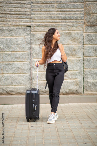 Full length happy young travel woman standing with suitcase