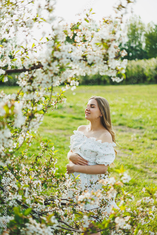 A young pregnant woman in a white dress walks in a blossoming apple orchard. Happy pregnant woman. Happy future mother A young pregnant woman in a white dress walks in a blossoming apple orchard. Happy pregnant woman. Happy future mother