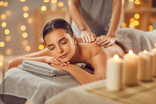 Young woman having back massage in beauty spa salon. Serene beautiful relaxed woman lying on couch with closed eyes receiving and enjoying relaxing massage. Beauty treatment, body care