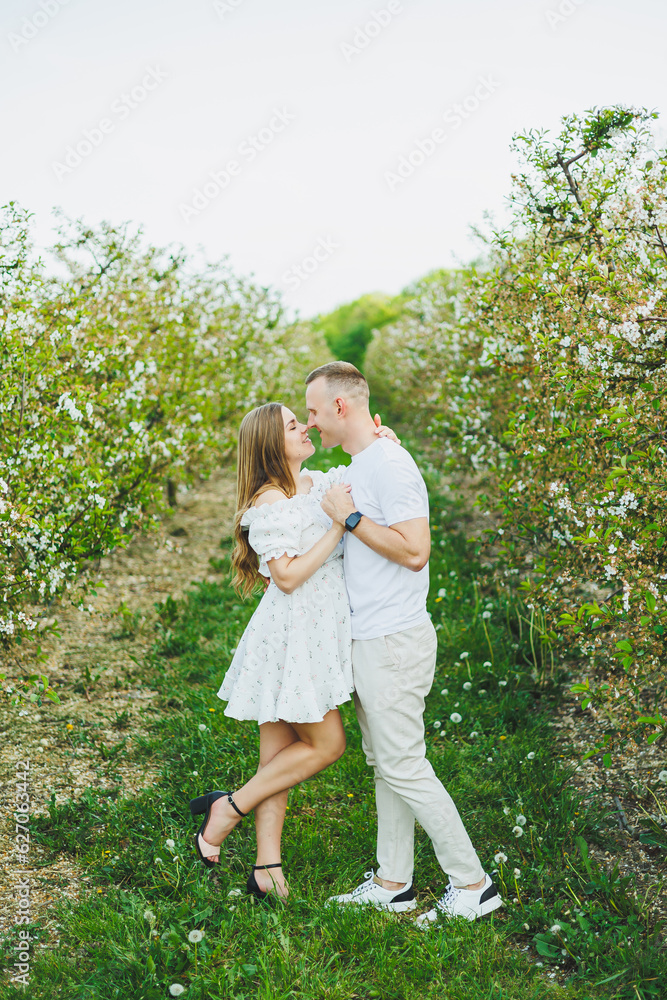 Beautiful young couple man and pregnant woman in spring garden. Beauty lifestyle family concept. A happy mother is expecting a baby. A happy young couple in a blooming garden Beautiful young couple man and pregnant woman in spring garden. Beauty lifestyle family concept. A happy mother is expecting a baby. A happy young couple in a blooming garden