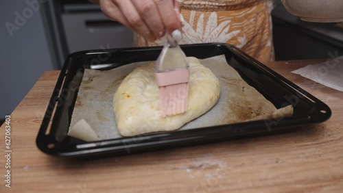 A woman uses a silicone brush to coat the Adjaran Khachapuri with oil, ensuring a golden crust. photo