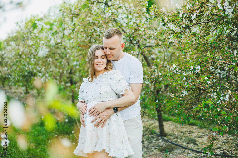 Beautiful young couple man and pregnant woman in spring garden. Beauty lifestyle family concept. A happy mother is expecting a baby. A happy young couple in a blooming garden Beautiful young couple man and pregnant woman in spring garden. Beauty lifestyle family concept. A happy mother is expecting a baby. A happy young couple in a blooming garden