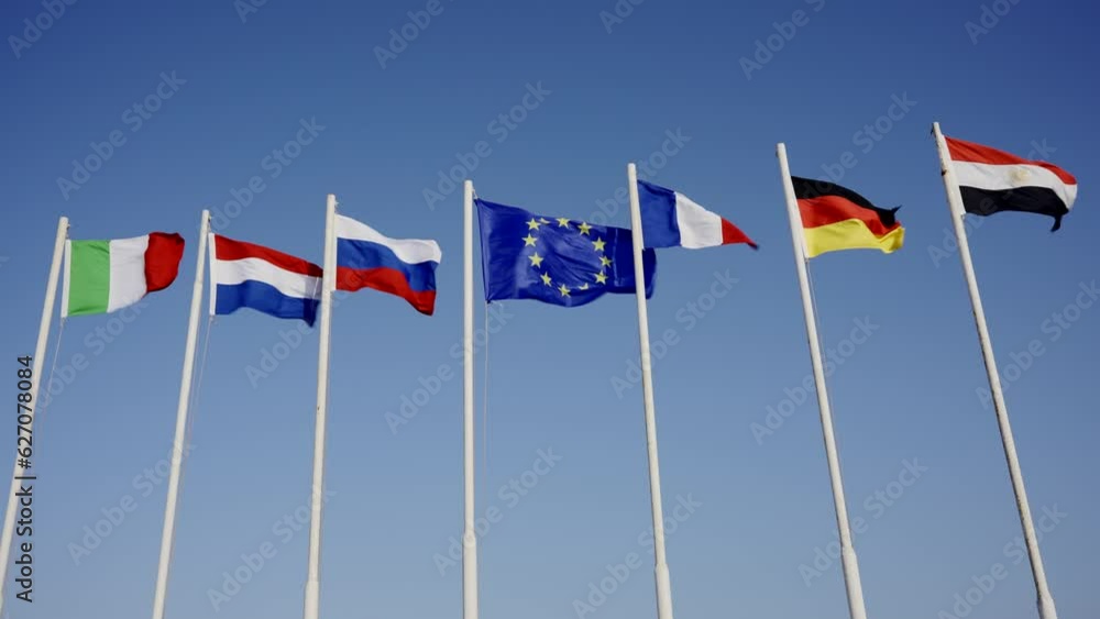Flags on flagpoles of different countries wavings on blue sky background Flags on flagpoles of different countries wavings on blue sky background