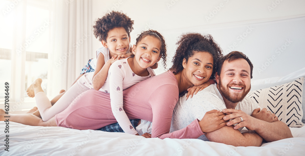 Interracial, happy family and portrait on a bed, bond and having fun on the weekend in their home together. Relax, love and face of playful children with parents in a bedroom, smile and playing games