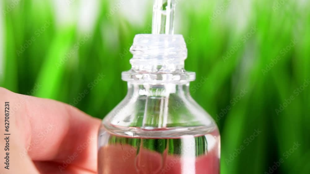 Extreme close up oil Bottle with a cosmetic pipette. glass bottle macro close-up isolated with green grass background.female hands takes a droplet of essential oil Extreme close up oil Bottle with a cosmetic pipette. glass bottle macro close-up isolated with green grass background.female hands takes a droplet of essential oil