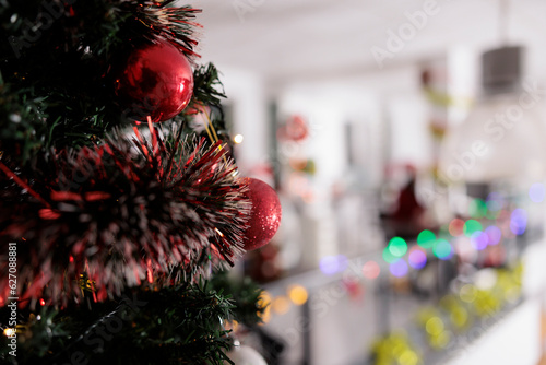 Close up focus on christmas tree decorated in red with modern office blurry in background. Ornate professional workplace ready for holiday season secret santa corporate party
