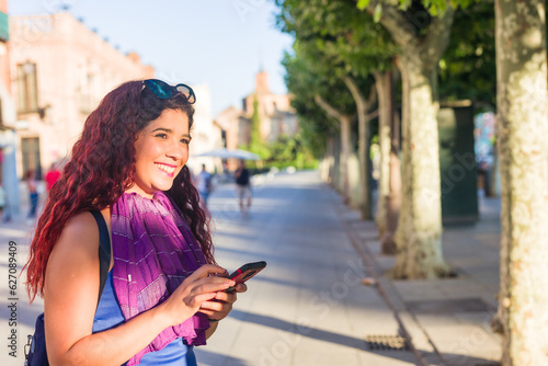 Alcala de Henares. Latin mid-woman travel holiday lifestyle portrait happy with smartphone in Spain