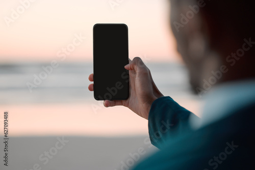 Businessman, hands and phone screen on beach for communication, advertising or outdoor networking. Closeup of man with mobile smartphone app display mockup by ocean coast for business trip or travel